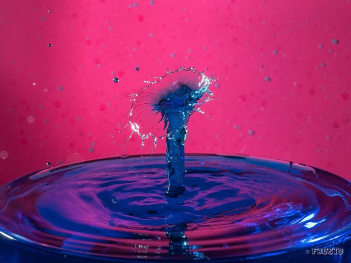 Close-up of drop falling on water against red background