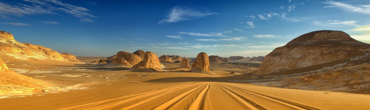 Panoramic view of tire tracks through desert