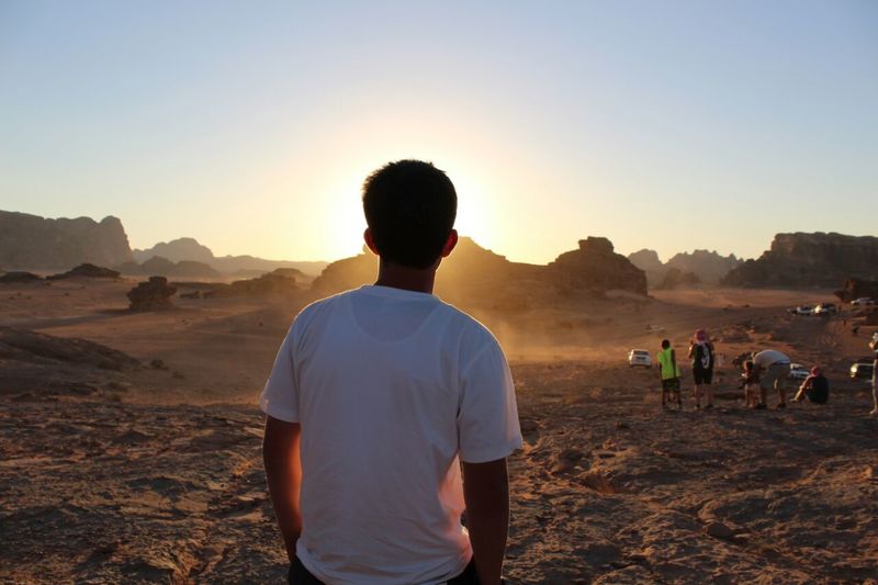 Rear view of man standing at desert during sunset