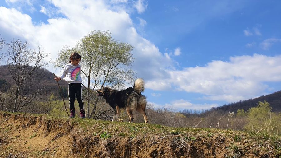 Girl with dog standing on land against sky