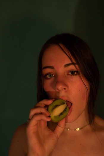 Portrait of woman eating kiwi fruit in darkroom