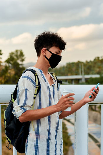 Young man using mobile phone against sky