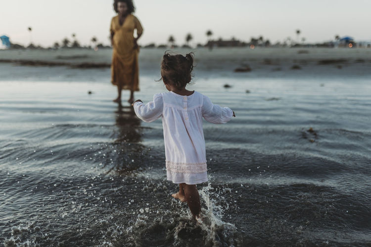 Young toddler girl splashing in the sea with family negative space