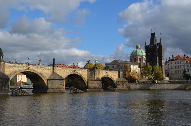 Arch bridge over river by buildings against sky in city