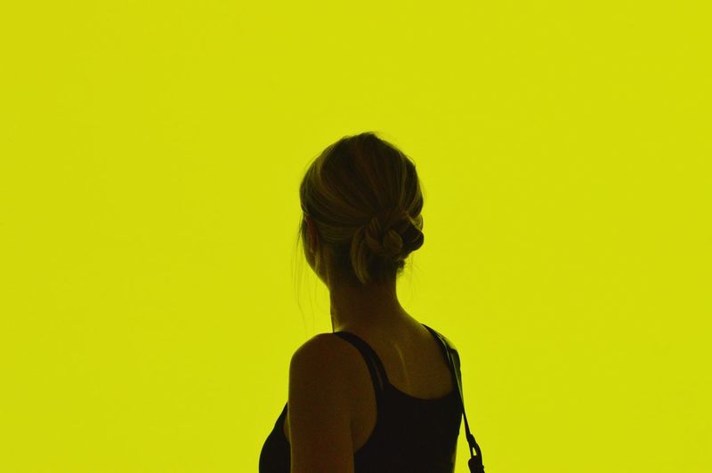 Close-up of woman standing against yellow background
