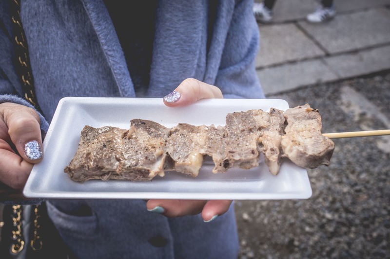 Midsection of woman holding meat in plate while standing at footpath