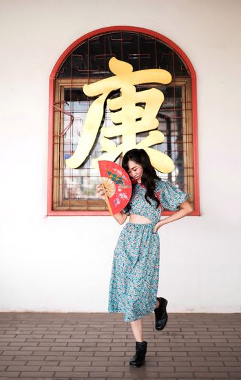 Portrait of woman in blue modern cheongsam holding a red fan at chinese temple 