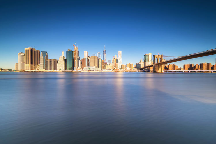 View of buildings by river against sky in city