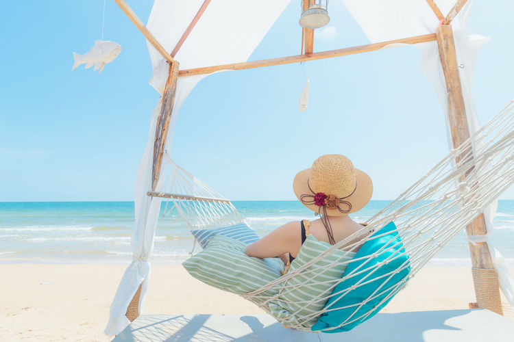 Woman sitting on beach umbrella by sea against sky
