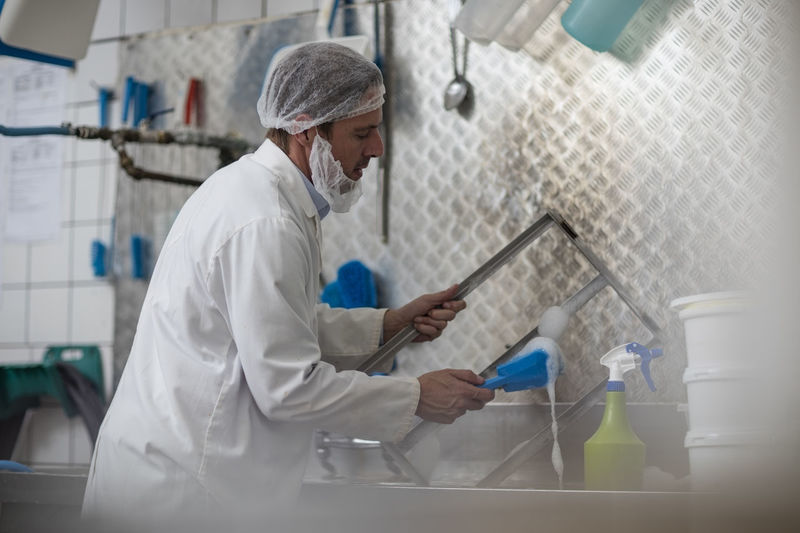 Cheese factory worker cleaning container parts