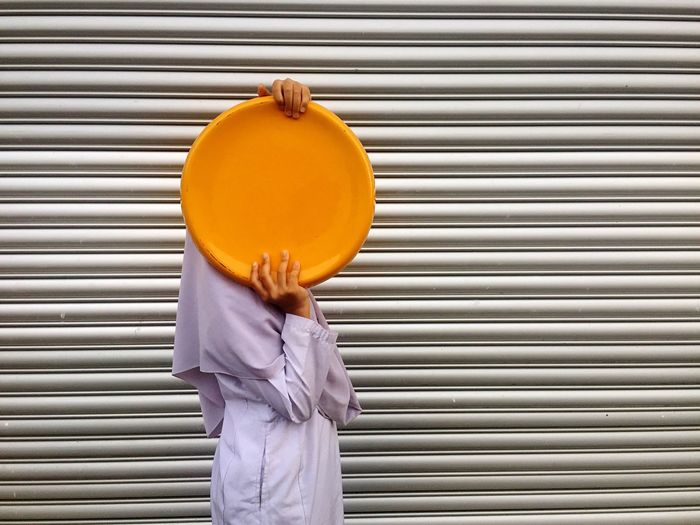 Side view of woman holding yellow metal plate against shutter