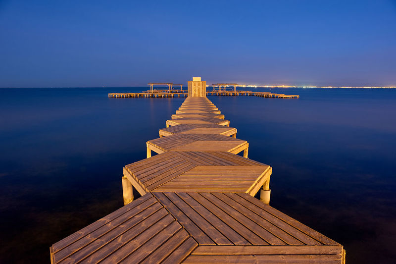 Pier over sea against clear blue sky