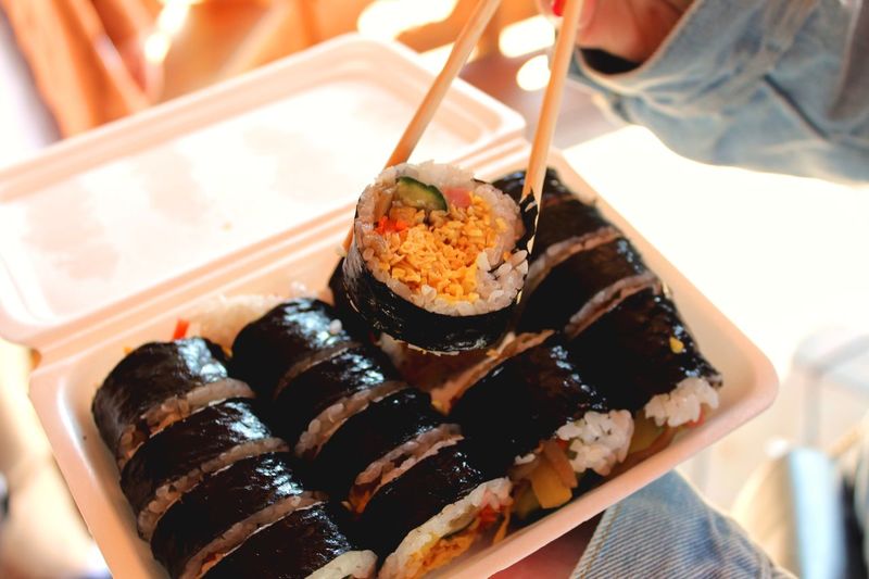 Cropped image of person using chopsticks while having sushi from container