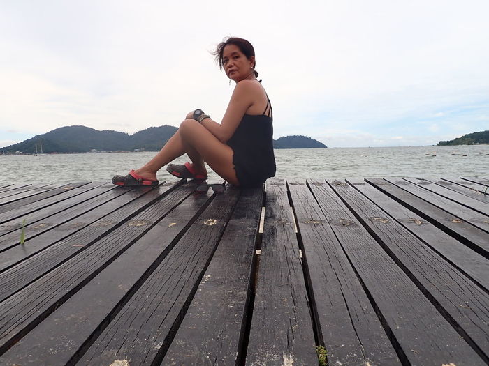 Woman sitting on wooden pier against sky