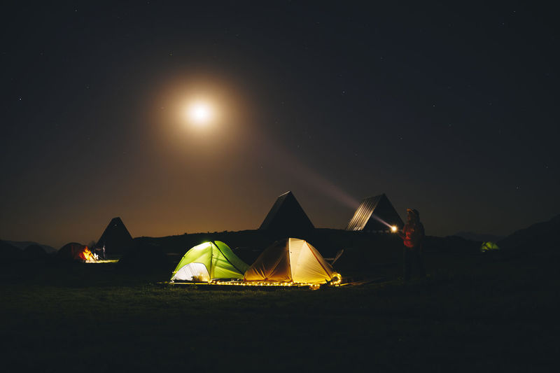 Tourist with flashlight standing near illuminated tents at caucasian state nature reserve in sochi, russia