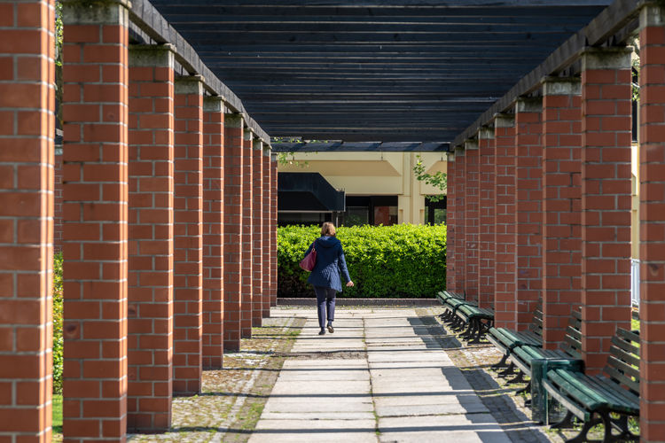 Rear view of woman walking on footpath amidst columns