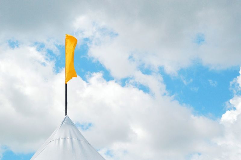 Low angle view of yellow flag on building against sky