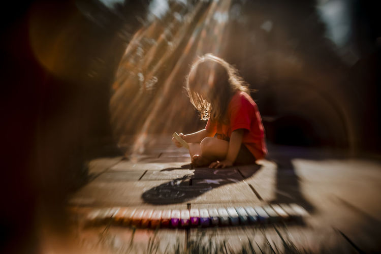 Girl drawing with colorful chalks on the patio during a summer evening
