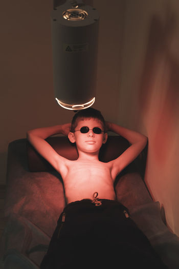 Boy lying under illuminated lighting equipment on bed