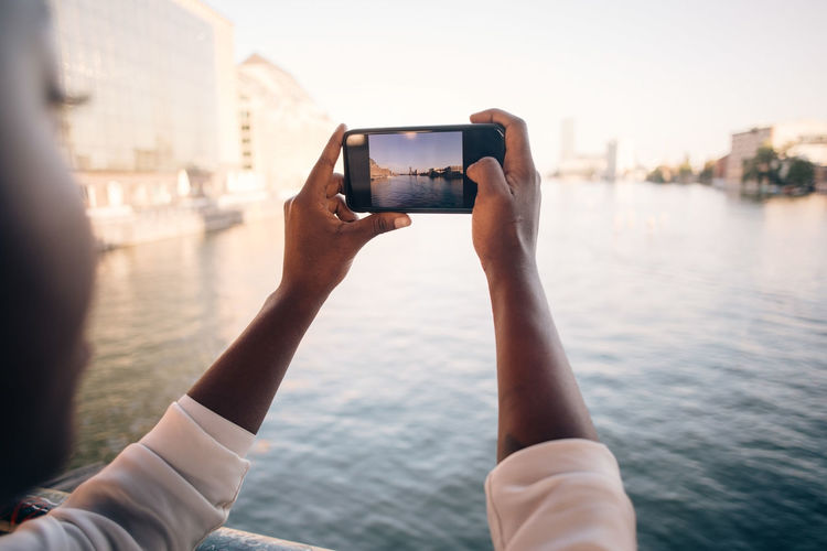 Close-up of man photographing river in city with mobile phone