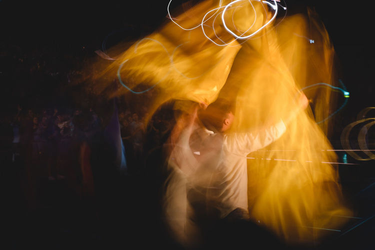 Rear view of man standing against black background dancing in long exposure shot