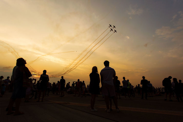 People watching airplane show against sky during sunset