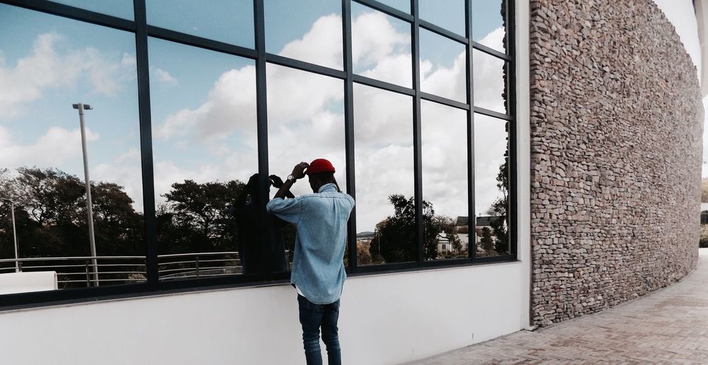 Reflection of man adjusting skull cap on modern building