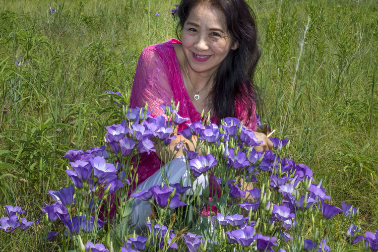 Portrait of smiling woman with purple flower in field
