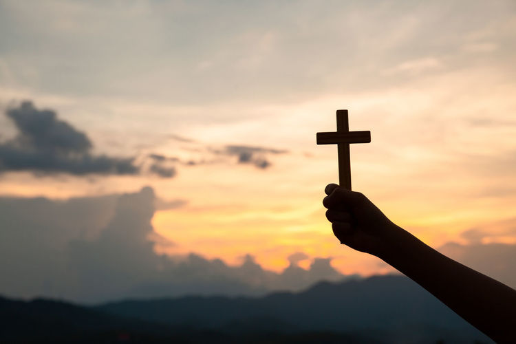 Hands holding wooden cross on sky background, crucifix, symbol of faith.