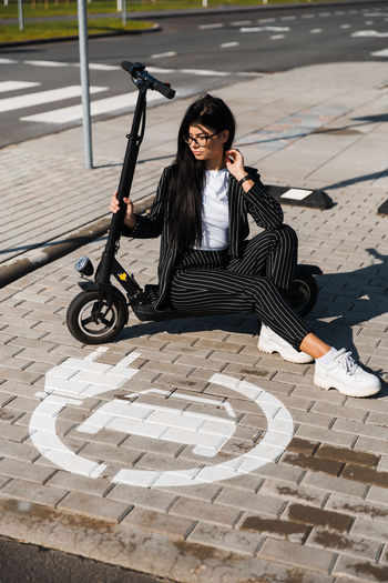 High angle view of woman with push scooter sitting on footpath