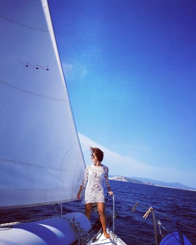 Woman standing on sailboat in sea against blue sky