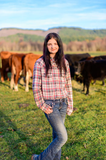 Portrait of young woman standing on field with cattle