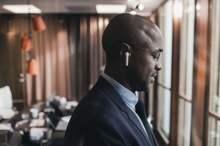 Profile view of bald businessman wearing in-ear headphones in board room at office