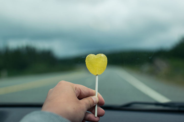 Close-up of cropped hand holding yellow heart shaped lollipop in car