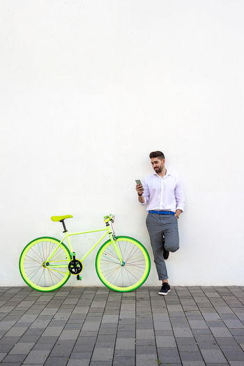Portrait of young man with bicycle standing against wall