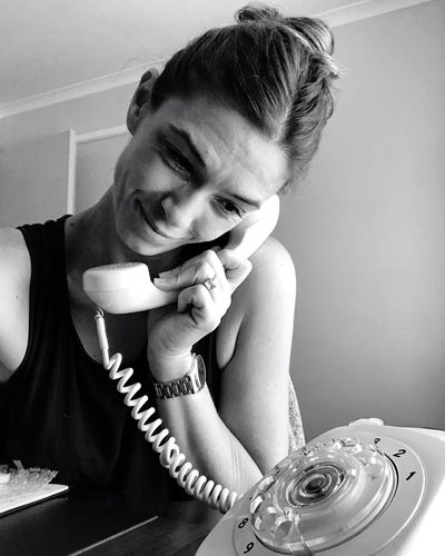 Smiling woman talking on old-fashioned rotary phone at home