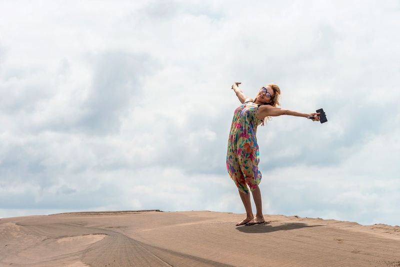 Blonde smiling woman gesturing happiness on the top of a sand dune