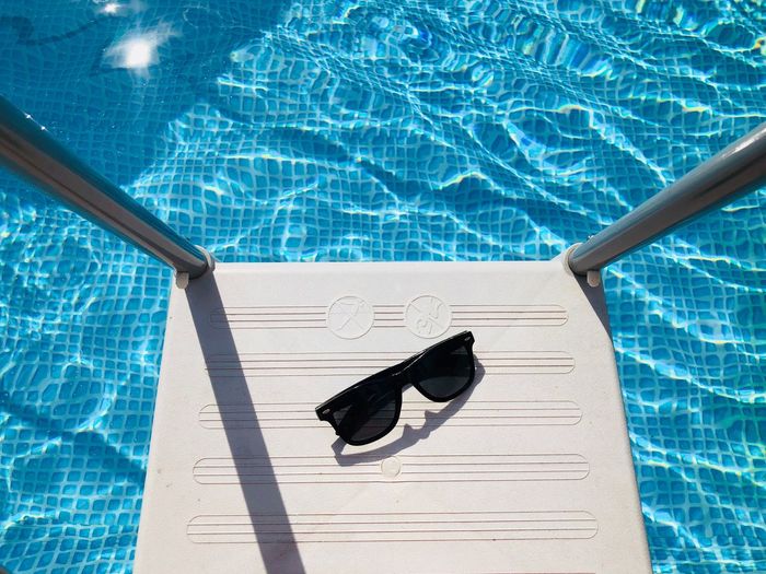 High angle view of sunglasses on ladder over swimming pool during sunny day