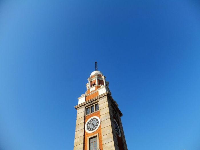 Low angle view of clock tower against clear blue sky on sunny day
