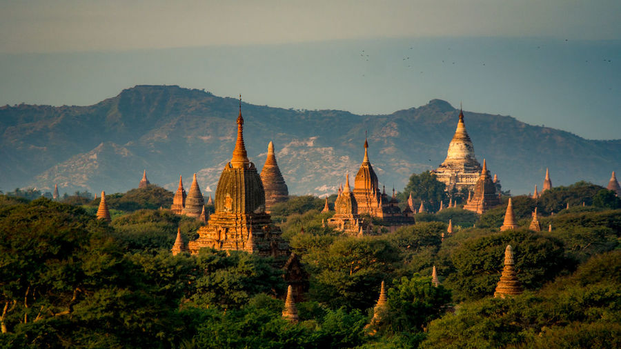 Old buddhist temples by mountains against sky during sunset