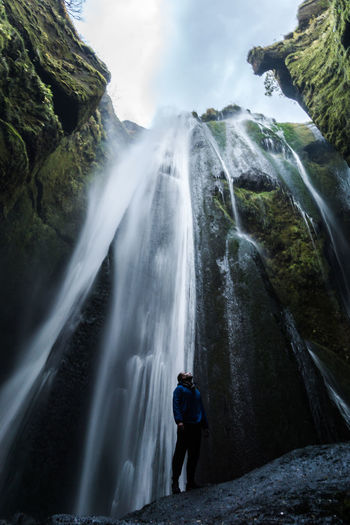 Low angle view of hiker standing against waterfall