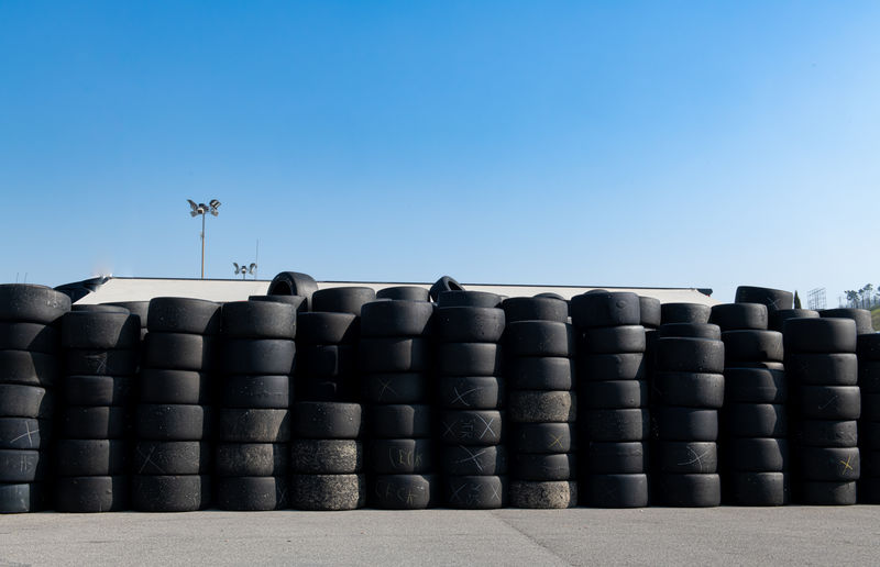 Large group of used old slick racing tire stacked against blue sky