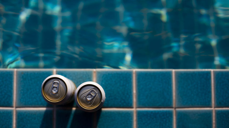 Selective focus two white beer cans are placed at the edge of the pool with space for text input.