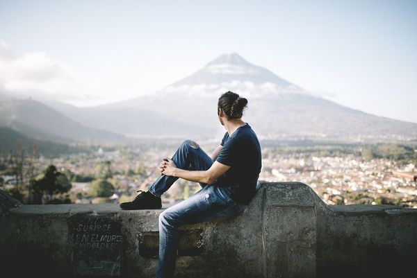 Side view of young man sitting on retaining wall against mountain