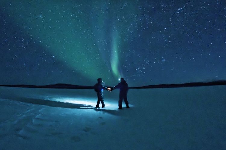 People on snowy land against sky at night