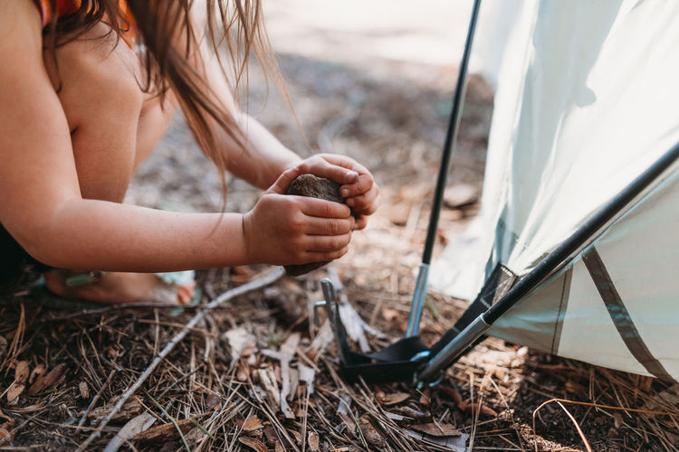 Cropped image of girl hitting stone on tent peg at campsite