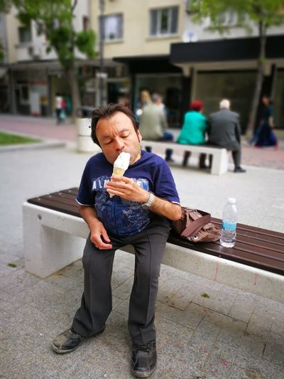 Dwarf man eating ice cream while sitting on bench