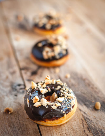 Close-up of chocolate glazed donuts with hazelnuts on wooden background
