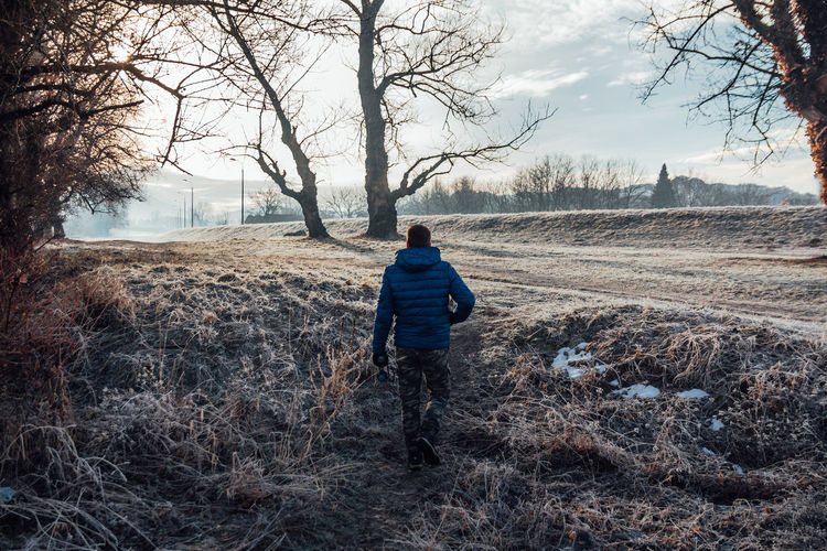 Rear view of man walking on field against sky