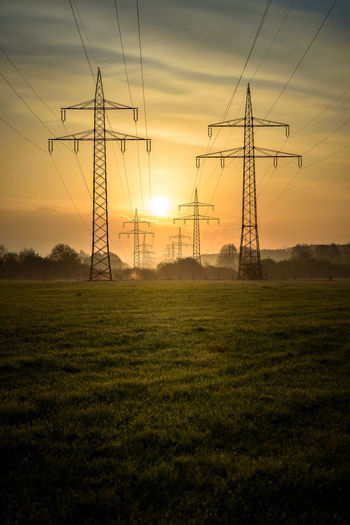 Electricity pylon on field against sky during sunset